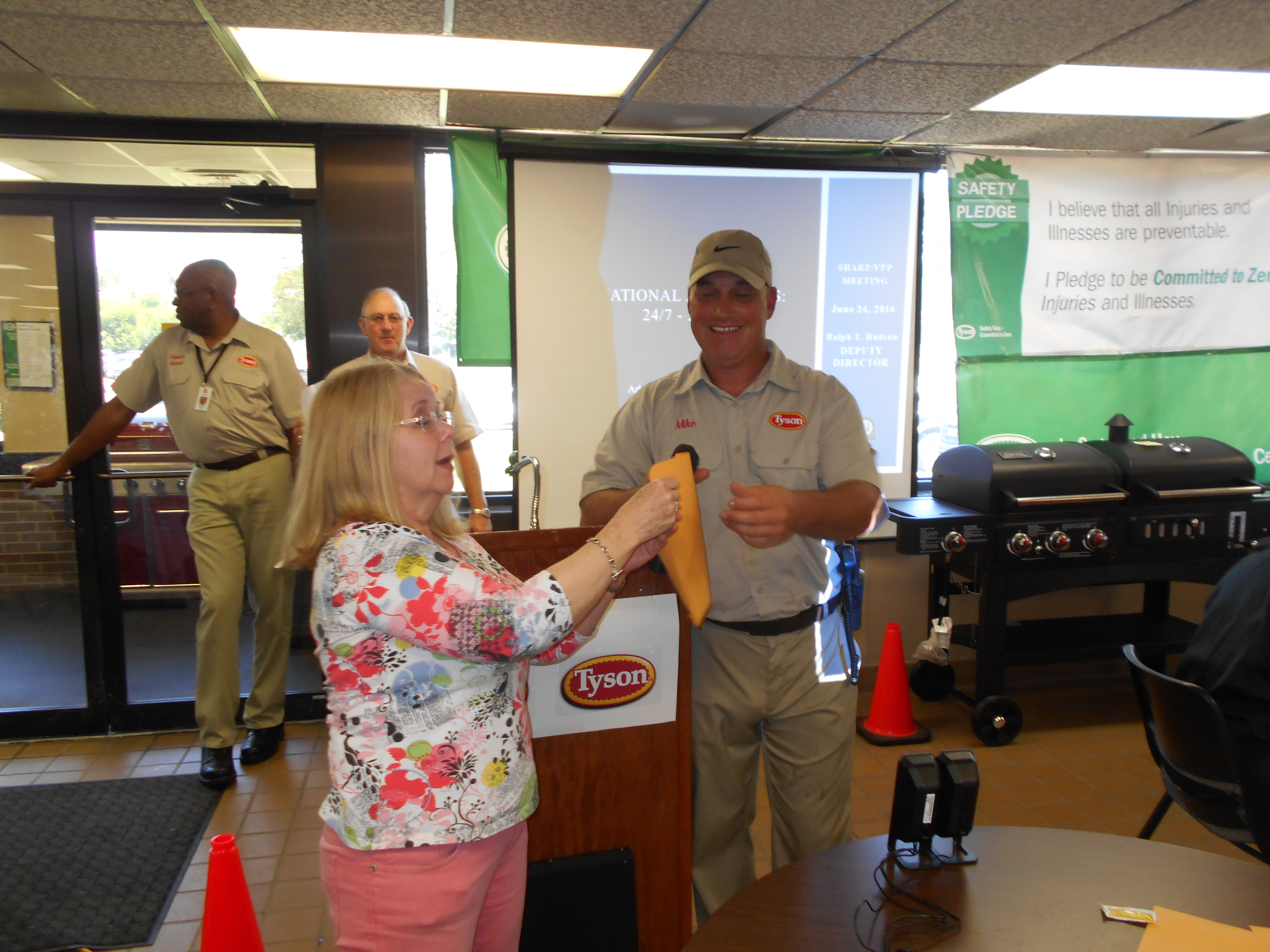 Pat Hart, director of the Health and Safety Division of the Arkansas Workers’ Compensation Commission, draws a winner’s name from an envelope held by Tyson plant manager Mike Hanson. Tyson gave away 20 flatscreen TV sets and eight deluxe barbecue grills in drawings to shift workers.